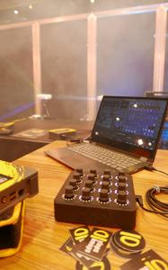 Ein Laptop mit angeschlossenem Midi-interface im Vordergrund. Zwei Minibeamer, die im Nebel Muster projezieren, im Hintergrund.